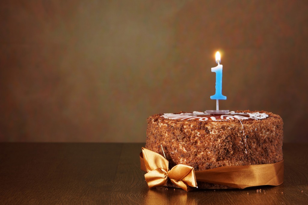 Birthday chocolate cake with burning candle as a number one on brown background