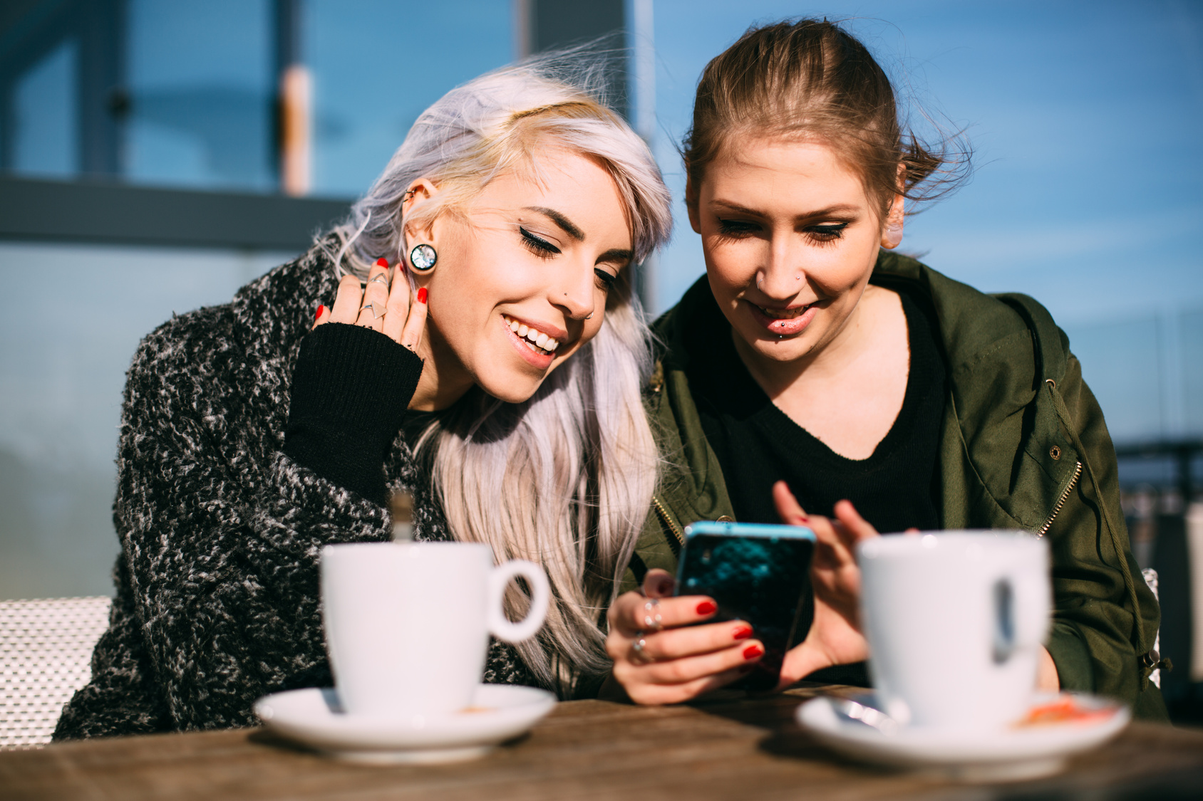Cool fashionable girls using smartphone in coffee shop