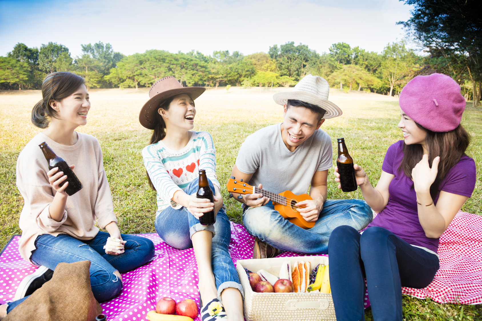 happy young friends enjoying picnic and playing ukulele